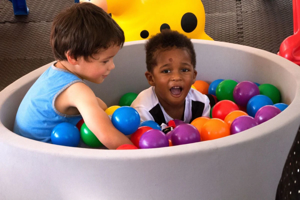 Two children laughing and playing together in a colourful ball pit